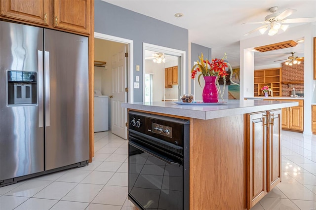 kitchen with black oven, washer / clothes dryer, stainless steel fridge with ice dispenser, light countertops, and light tile patterned floors