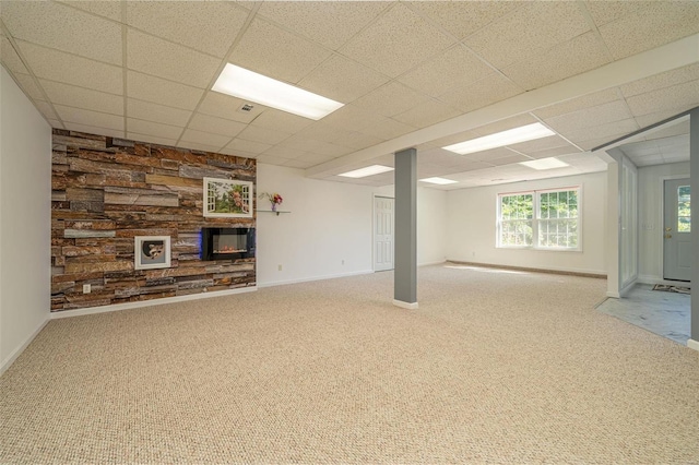 below grade area featuring a stone fireplace, baseboards, carpet, and a drop ceiling