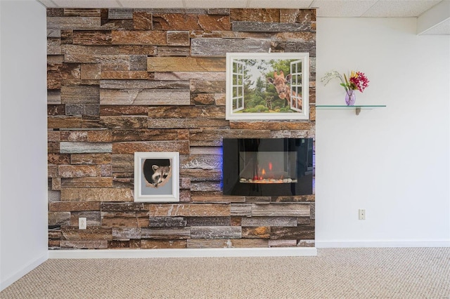 interior details with carpet flooring, a paneled ceiling, baseboards, and a glass covered fireplace