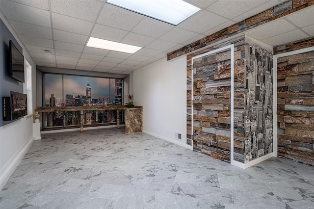 interior space with a drop ceiling, baseboards, marble finish floor, and visible vents