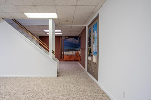 hallway with carpet flooring, a paneled ceiling, and baseboards