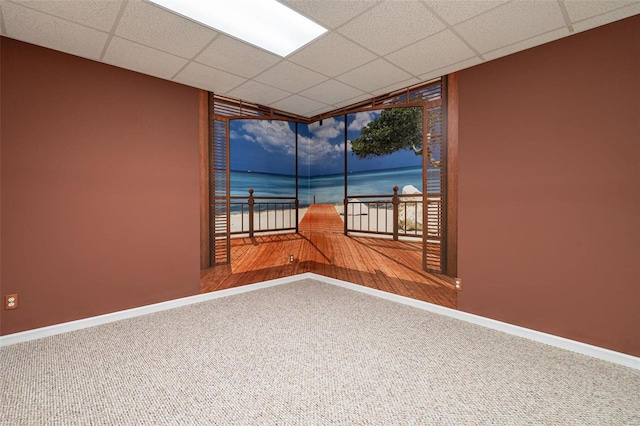 carpeted empty room with a drop ceiling and baseboards