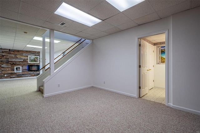 finished below grade area with visible vents, baseboards, carpet, a paneled ceiling, and stairs