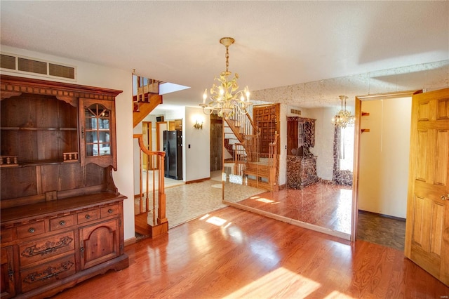 unfurnished dining area with a textured ceiling, a chandelier, and hardwood / wood-style floors