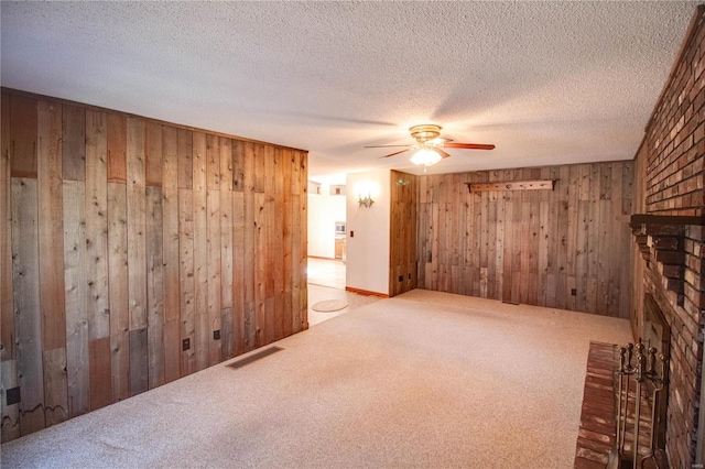 unfurnished room with a fireplace, wooden walls, carpet flooring, ceiling fan, and a textured ceiling