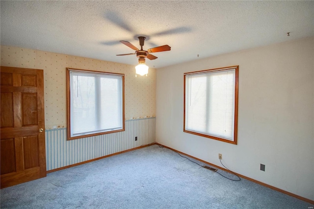 carpeted spare room with a textured ceiling, plenty of natural light, and ceiling fan