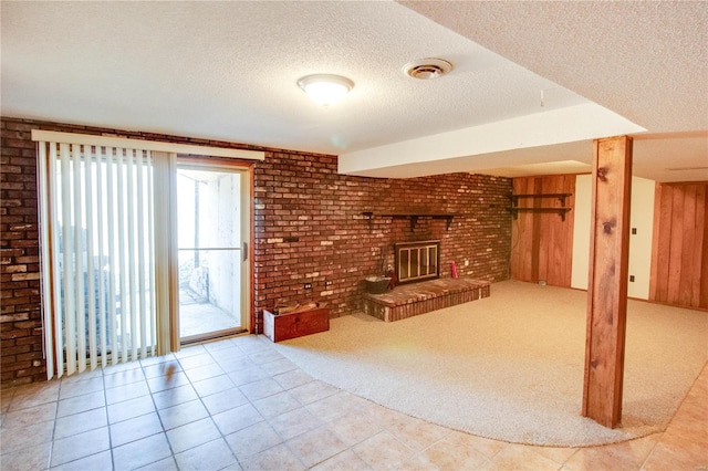 unfurnished living room featuring light carpet, a textured ceiling, a fireplace, and brick wall