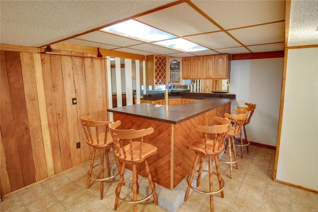 kitchen featuring wood walls, a kitchen breakfast bar, kitchen peninsula, and light tile patterned flooring