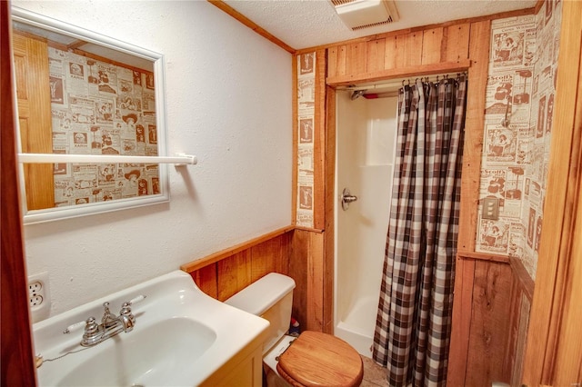 bathroom with a textured ceiling, vanity, walk in shower, toilet, and wooden walls