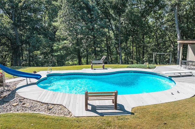 view of pool with a water slide, a wooden deck, a lawn, and a diving board