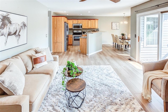 living room with light wood-type flooring and ceiling fan with notable chandelier