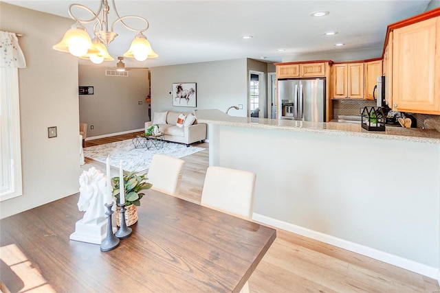 kitchen with an inviting chandelier, light hardwood / wood-style flooring, hanging light fixtures, stainless steel appliances, and decorative backsplash