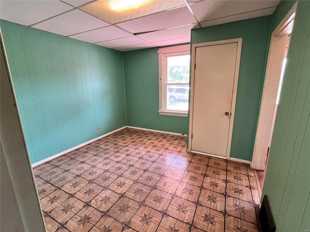 spare room with a paneled ceiling and wood walls