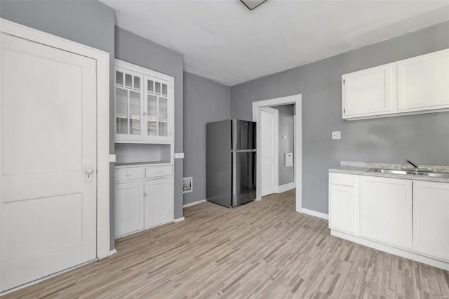 kitchen featuring light wood-type flooring, stainless steel fridge, sink, and white cabinets