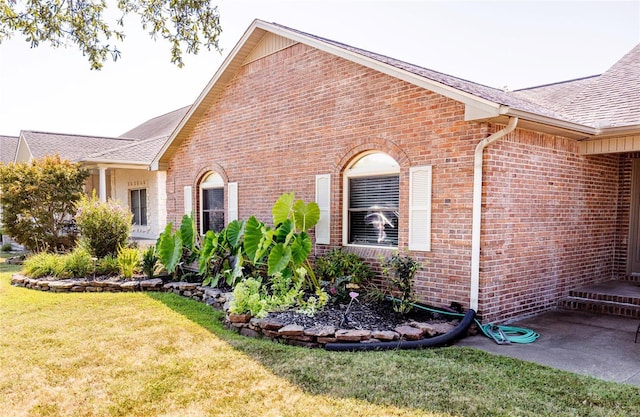 view of side of property featuring brick siding, a lawn, and roof with shingles