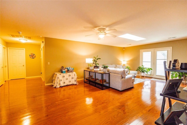 living room featuring a skylight, wood finished floors, baseboards, and ceiling fan