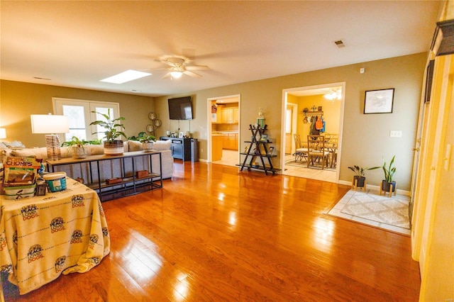 living room with visible vents, a ceiling fan, wood finished floors, a skylight, and baseboards