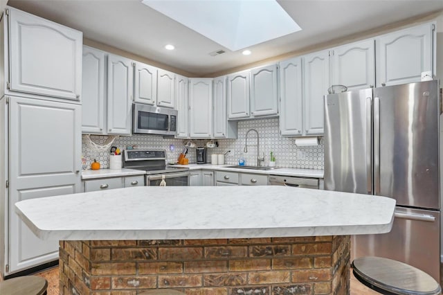 kitchen with decorative backsplash, sink, a skylight, a kitchen island, and appliances with stainless steel finishes