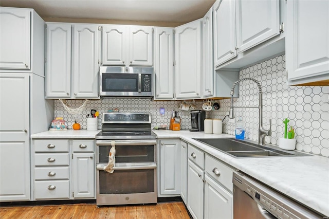 kitchen featuring backsplash, white cabinets, light hardwood / wood-style floors, and stainless steel appliances