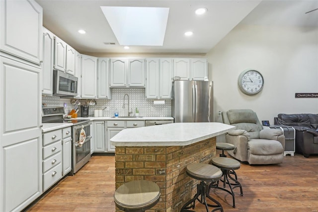 kitchen featuring light hardwood / wood-style floors, sink, a breakfast bar, white cabinetry, and appliances with stainless steel finishes