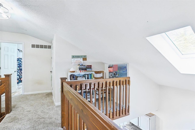 hall featuring light colored carpet, a textured ceiling, and lofted ceiling with skylight