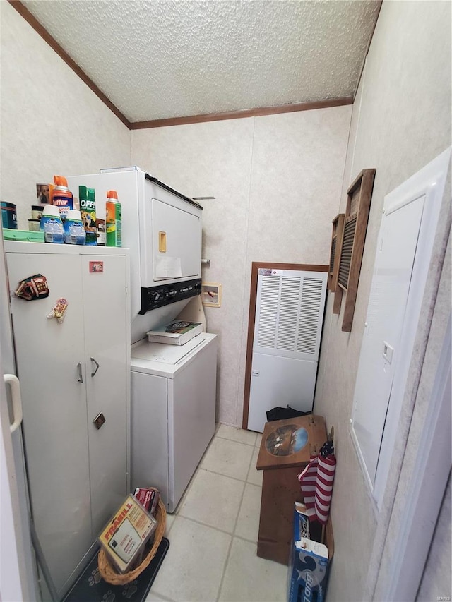 laundry area featuring light tile patterned floors, stacked washer and clothes dryer, crown molding, and a textured ceiling