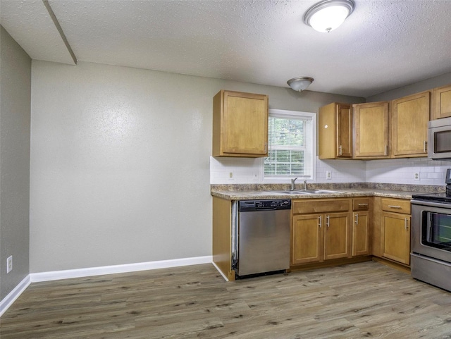 kitchen with light wood-type flooring, a textured ceiling, stainless steel appliances, and sink