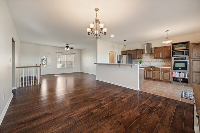 kitchen with wall chimney range hood, a breakfast bar area, hanging light fixtures, hardwood / wood-style floors, and appliances with stainless steel finishes