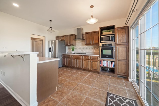 kitchen featuring a breakfast bar area, appliances with stainless steel finishes, plenty of natural light, pendant lighting, and wall chimney exhaust hood