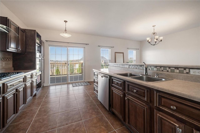 kitchen with dark tile patterned flooring, sink, hanging light fixtures, stainless steel appliances, and decorative backsplash