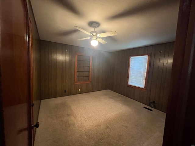 carpeted empty room with wood walls and ceiling fan