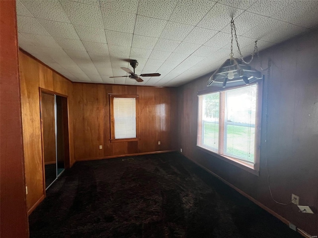 unfurnished room featuring dark carpet, ceiling fan, and wood walls