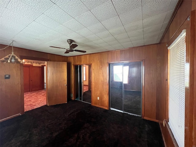 unfurnished bedroom featuring ceiling fan, dark colored carpet, and wooden walls