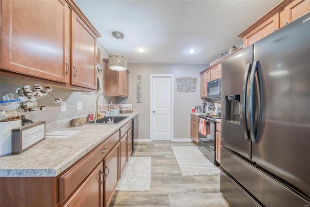 kitchen featuring sink, light hardwood / wood-style flooring, hanging light fixtures, and black appliances