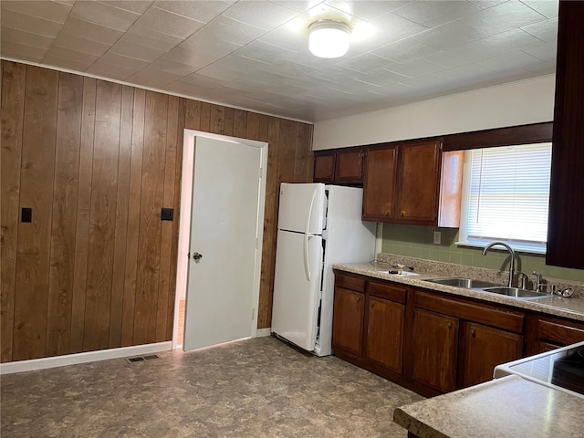 kitchen with white refrigerator, sink, wooden walls, and range