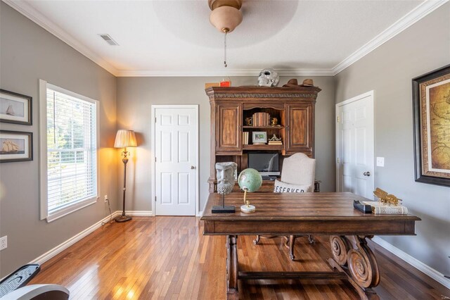 home office featuring visible vents, crown molding, baseboards, light wood-type flooring, and a ceiling fan