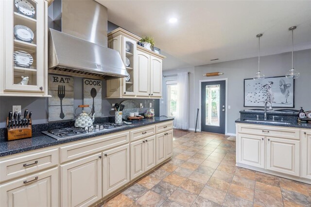 kitchen with stainless steel gas stovetop, glass insert cabinets, wall chimney exhaust hood, and a sink