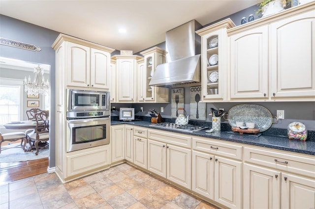 kitchen with glass insert cabinets, cream cabinetry, appliances with stainless steel finishes, and wall chimney exhaust hood