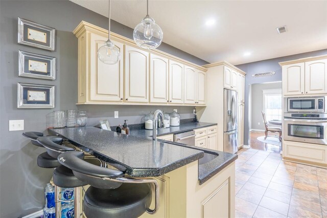 kitchen featuring visible vents, decorative light fixtures, a peninsula, cream cabinetry, and stainless steel appliances