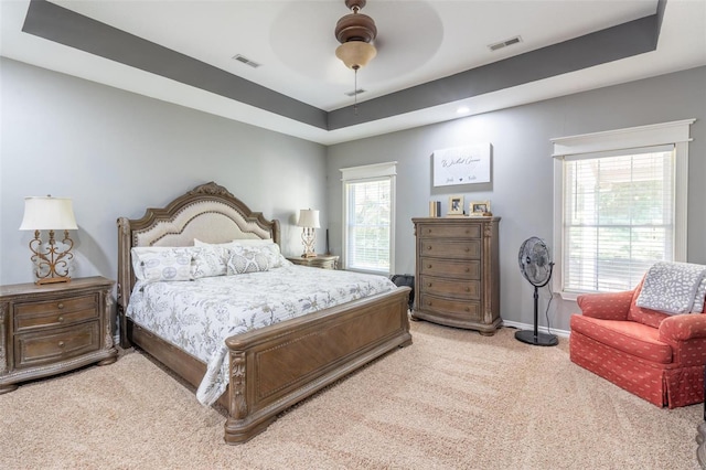 bedroom featuring light carpet, visible vents, baseboards, and a tray ceiling