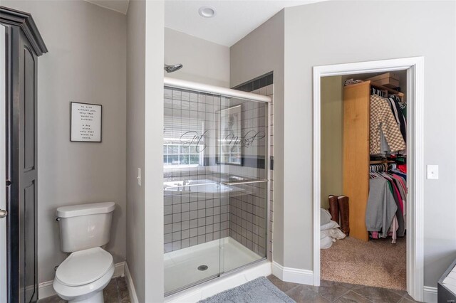 full bathroom with a shower stall, toilet, a walk in closet, and baseboards