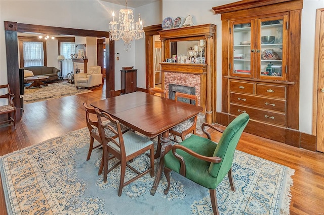 dining area featuring wood-type flooring, a brick fireplace, and a chandelier