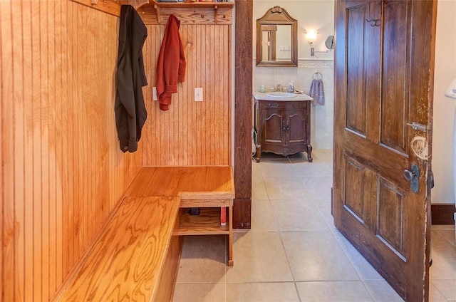 mudroom featuring light tile patterned floors, wooden walls, and sink