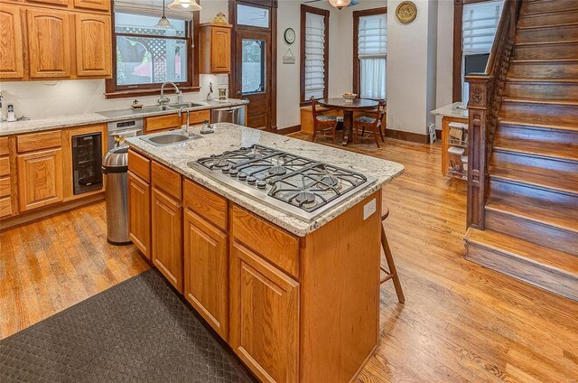 kitchen featuring light wood-type flooring, stainless steel appliances, sink, an island with sink, and wine cooler