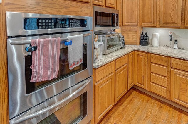 kitchen with light wood-type flooring, backsplash, stainless steel appliances, and light stone countertops