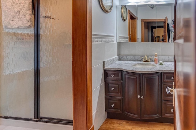 bathroom with hardwood / wood-style flooring, walk in shower, tile walls, decorative backsplash, and vanity