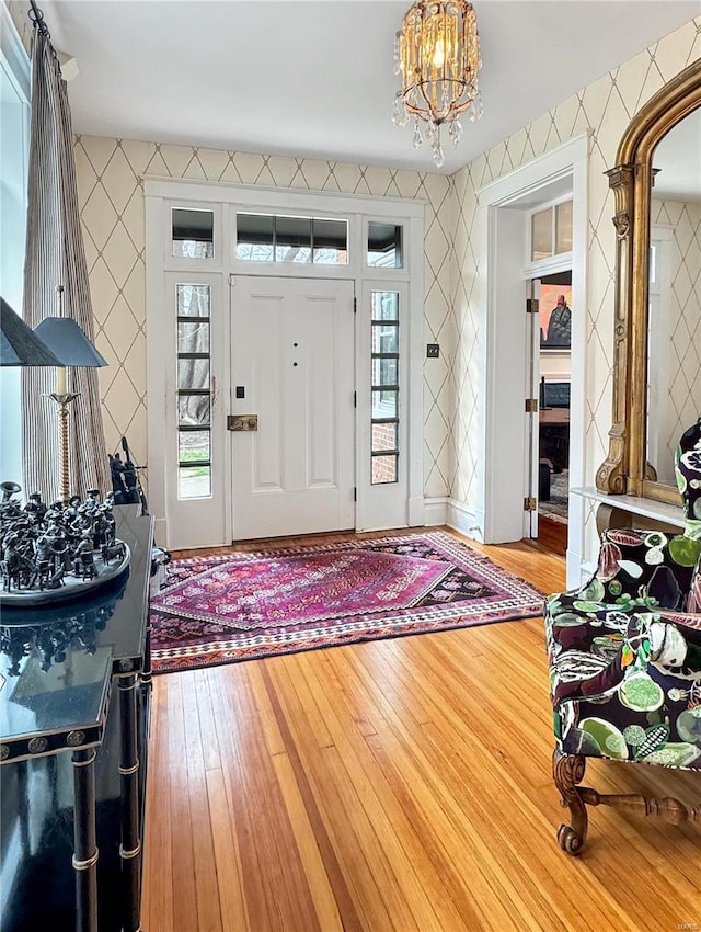 foyer with tile walls, a chandelier, hardwood / wood-style flooring, and ornate columns