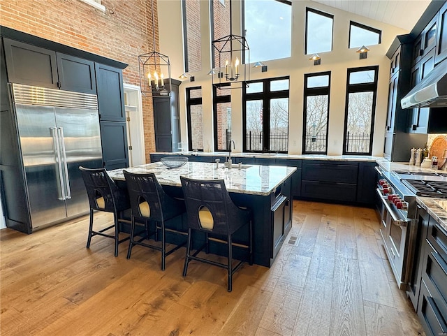 kitchen featuring a kitchen island with sink, light hardwood / wood-style flooring, a high ceiling, and high quality appliances