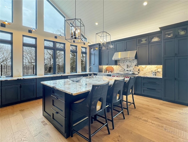 kitchen with light stone countertops, light hardwood / wood-style floors, an island with sink, a breakfast bar area, and decorative backsplash