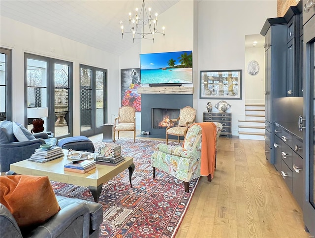 living room with high vaulted ceiling, a notable chandelier, light wood-type flooring, and a fireplace